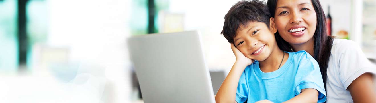 Young boy sitting at laptop with adult woman smiling 